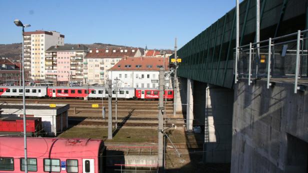 Ein Cityshuttle-Zug steht auf einem Bahnhofsgleis vor Wohngebäuden.
