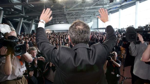Ein Mann steht vor einer großen Menschenmenge und hebt die Arme.