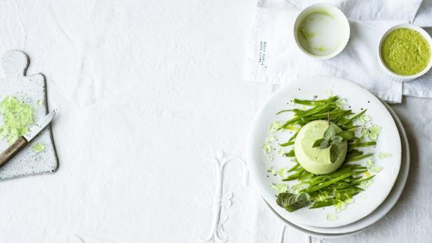 Ein grünes Gemüsegericht mit Bohnen und Minze auf einem weißen Teller.