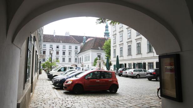 Blick durch einen Torbogen auf einen Platz mit geparkten Autos in Wien.