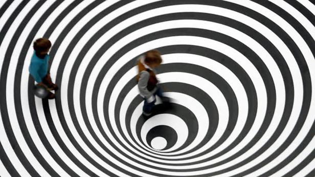 Zwei Kinder laufen über einen Boden mit einem schwarz-weißen Spiralmuster.