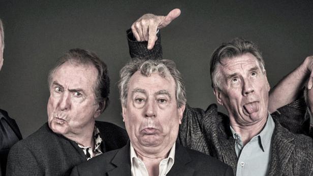 Fünf Männer posieren mit lustigen Gesichtsausdrücken vor einem dunklen Hintergrund.