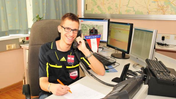 Ein lächelnder Mann in Polizei-Sportkleidung telefoniert und schreibt in einem Büro.