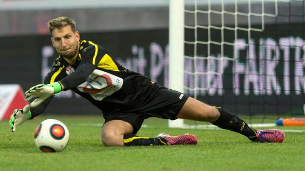 Ein Torwart hechtet nach einem Fußball vor einem Tornetz.