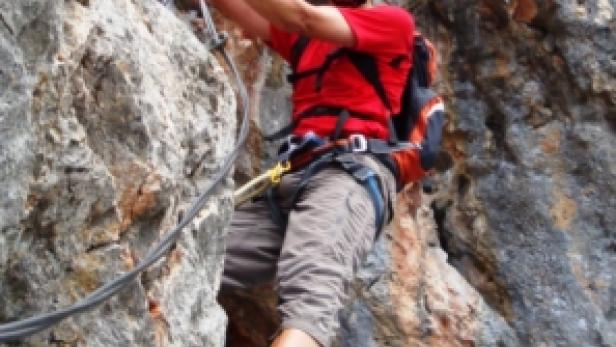 Ein Mann klettert mit Helm und Kletterausrüstung einen Felsen hoch.