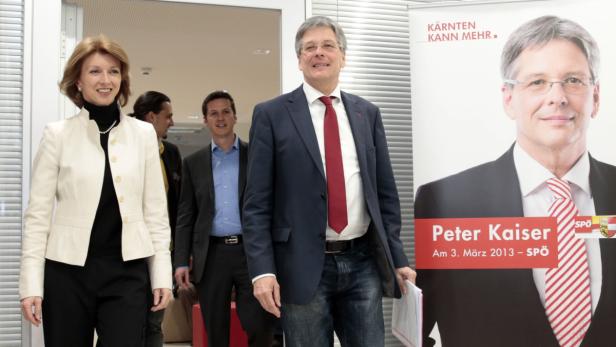 Eine Gruppe von Personen steht vor einem Wahlplakat von Peter Kaiser.