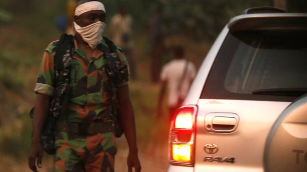 Ein Soldat mit Tarnuniform und Gesichtsmaske steht neben einem Toyota RAV4.