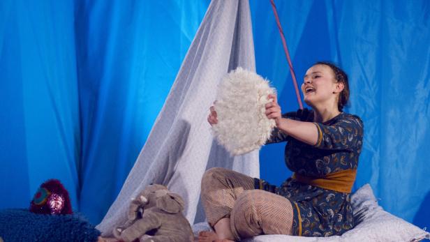 Eine junge Frau sitzt vor einem blauen Hintergrund und spielt mit einem weißen, flauschigen Gegenstand.