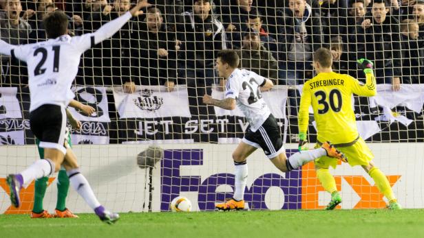 Ein Fußballspieler jubelt nach einem Tor, während der Torwart versucht, den Ball abzuwehren.