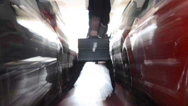 Eine Person mit einem Aktenkoffer geht zwischen zwei geparkten Autos hindurch.