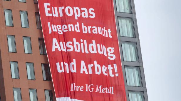 Ein rotes Banner an einem Gebäude fordert „Europas Jugend braucht Ausbildung und Arbeit! Ihre IG Metall.“.