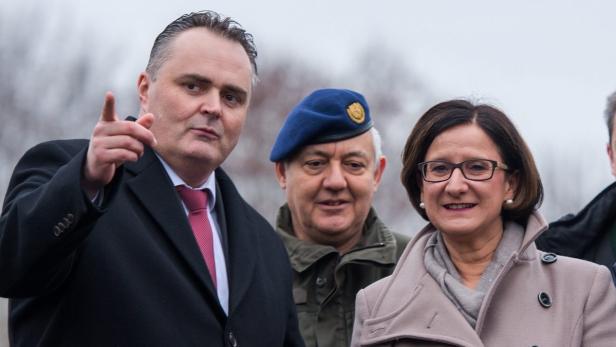 Drei Personen, darunter ein Mann im Anzug, ein Soldat mit Barett und eine Frau mit Brille, stehen zusammen.