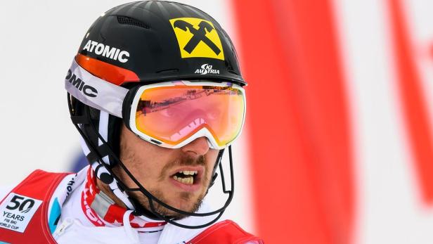 Ein Skirennläufer mit Helm und Skibrille vor einem roten Hintergrund.