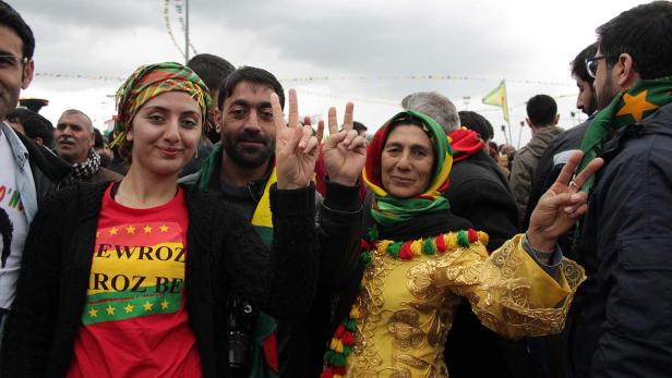 Eine Gruppe von Menschen feiert Newroz mit traditioneller Kleidung und Friedenszeichen.