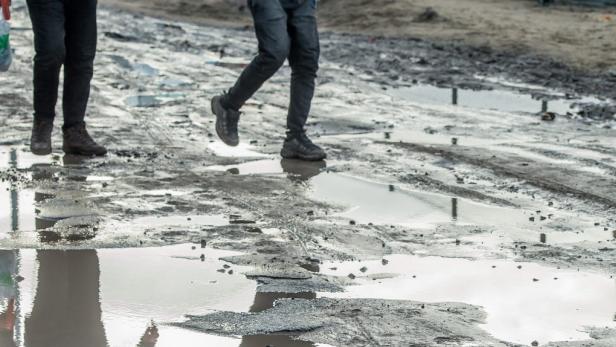 Zwei Personen gehen auf einer schlammigen Straße mit Pfützen.