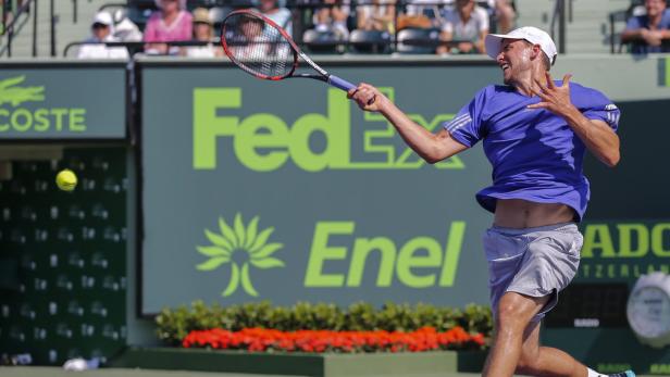 Ein Tennisspieler schlägt einen Ball vor einer Werbetafel.