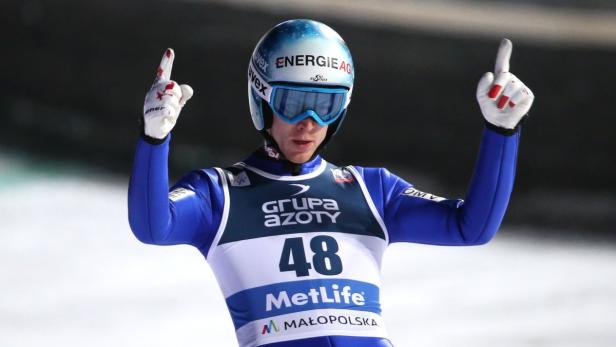 Ein Skispringer mit Helm und Brille jubelt mit erhobenen Zeigefingern.