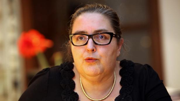 Eine Frau mit Brille und Goldkette schaut aufmerksam zur Seite.