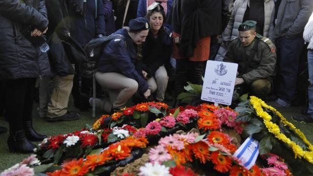 Trauernde knien vor einem mit Blumen geschmückten Grabstein.