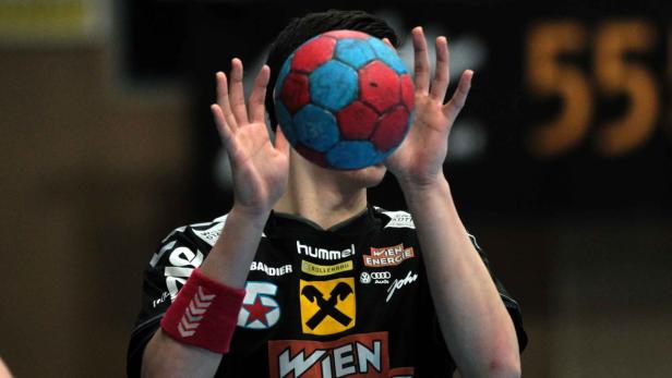 Ein Handballspieler hält einen rot-blauen Ball vor seinem Gesicht.