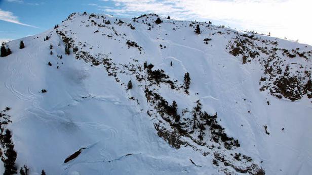 Ein schneebedeckter Berghang mit einigen Bäumen und Spuren im Schnee.