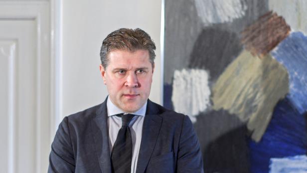 Ein Mann in Anzug und Krawatte steht vor einem abstrakten Gemälde.