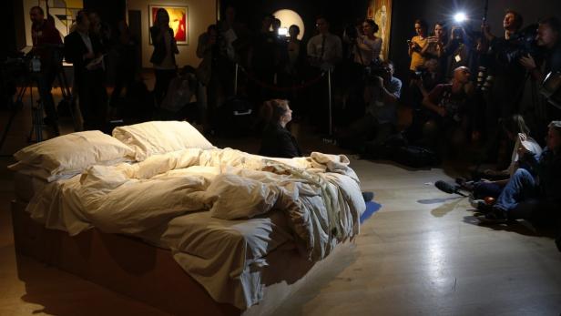 Ein ungemachtes Bett steht im Mittelpunkt einer Kunstausstellung, umringt von Fotografen.