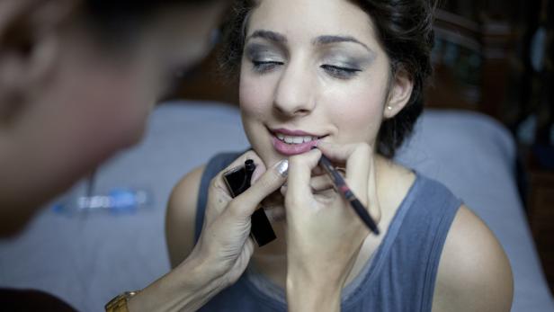 Eine Frau bekommt Lippenstift von einem Visagisten aufgetragen.
