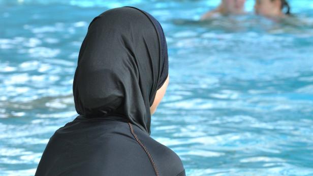 Eine Frau mit Burqini steht am Rand eines Schwimmbeckens.