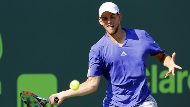 Ein Tennisspieler in einem blauen Hemd schlägt einen Tennisball.