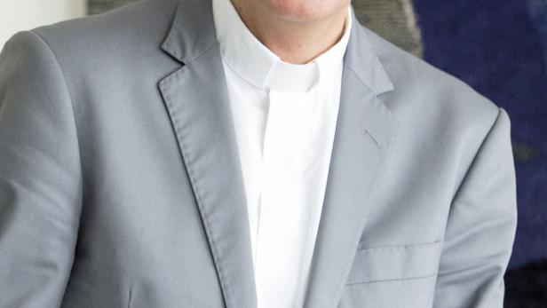 Ein lachender Mann mit grauem Haar trägt einen hellgrauen Anzug.
