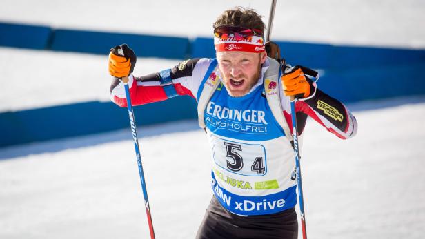 Ein Biathlet jubelt mit Skiern und Stöcken im Schnee.