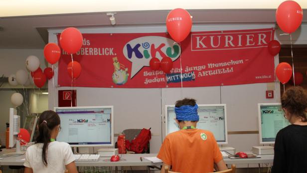 Kinder sitzen vor Computern unter einem Banner von „KiKu“ und „Kurier“.