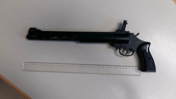 Ein schwarzer Revolver liegt neben einem Lineal.