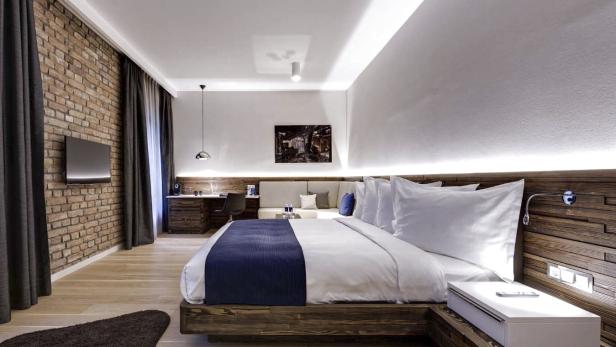 Ein modernes Schlafzimmer mit Holzboden, Ziegelwand und einem großen Bett mit blauer Tagesdecke.