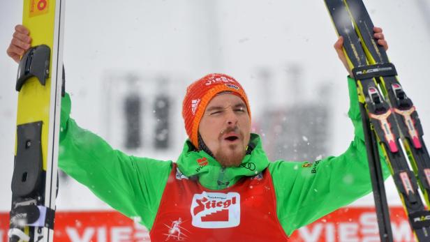 Ein Skispringer jubelt mit erhobenen Skiern im Schnee.