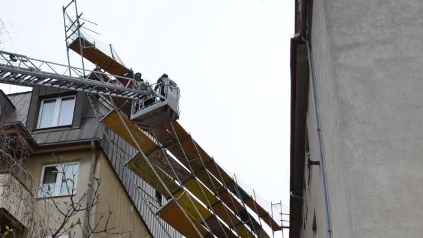 Ein Bauarbeiter in einem Hubsteiger inspiziert ein Gebäude mit einem Gerüst.