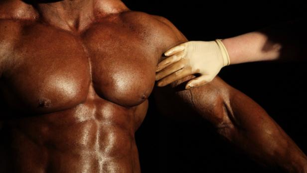 Der Oberkörper eines Bodybuilders wird von einer Hand mit einem Handschuh berührt.