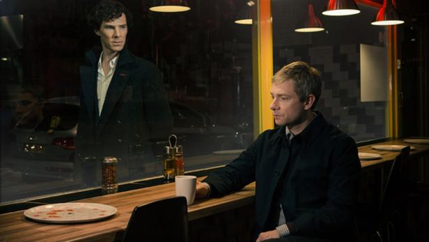 Martin Freeman sitzt in einem Restaurant, während Benedict Cumberbatch durch das Fenster zu sehen ist.