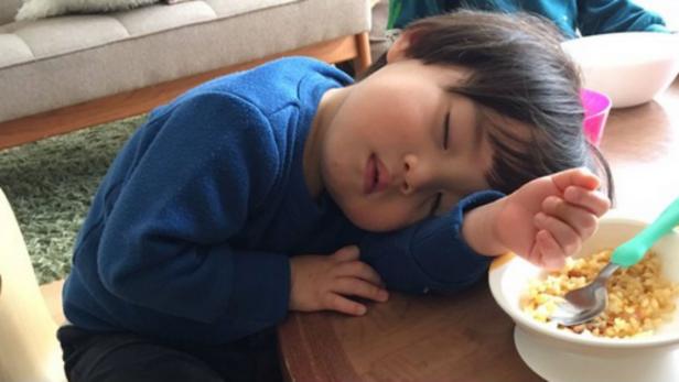 Ein kleiner Junge schläft am Tisch neben seinem Essen ein.