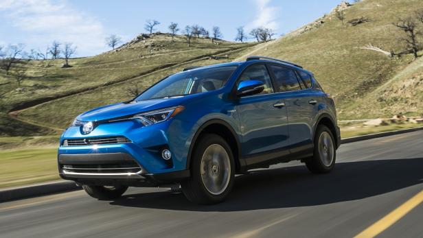 Ein blauer Toyota RAV4 fährt auf einer asphaltierten Straße an einem Hügel vorbei.