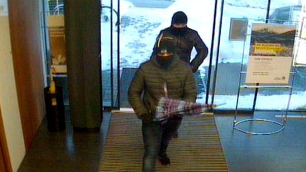 Zwei maskierte Personen betreten ein Gebäude.