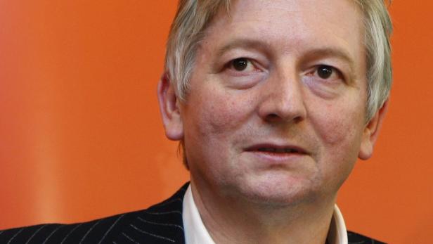 Porträt eines Mannes mit grauem Haar vor einem orangefarbenen Hintergrund.