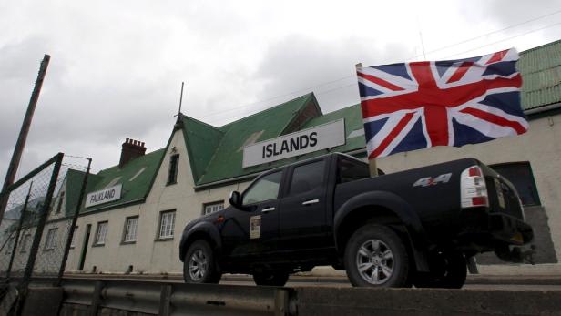 Ein schwarzer Pickup-Truck vor einem Gebäude mit der Aufschrift „Falkland Islands“ und einer britischen Flagge.