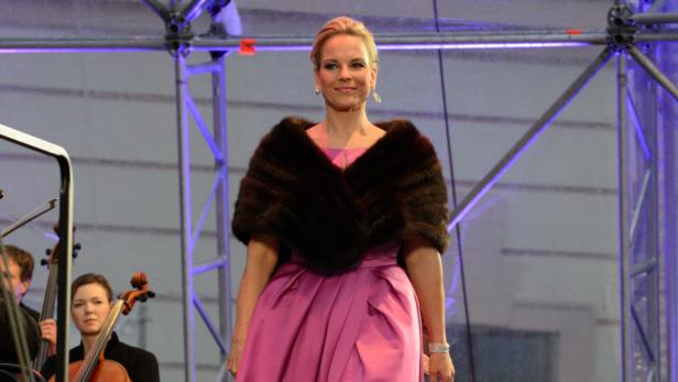 Eine Frau in einem rosa Kleid und einer Stola steht vor einem Orchester.