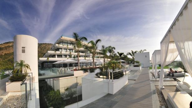 Ein modernes Hotelresort mit Palmen und Liegebereichen unter strahlend blauem Himmel.