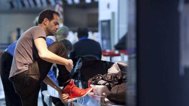 Ein Mann zieht seine roten Schuhe an einem Flughafen aus.
