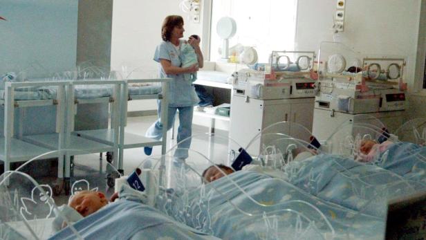 Eine Krankenschwester hält ein Baby in einem Raum mit mehreren Babybetten.