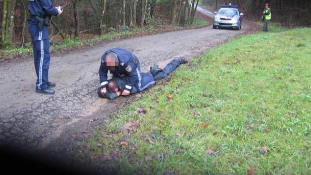 Ein Polizist fixiert eine Person am Boden, während ein anderer Polizist daneben steht.