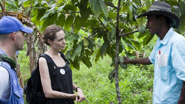 Angelina Jolie besucht eine Kakaoplantage und spricht mit einem lokalen Farmer.